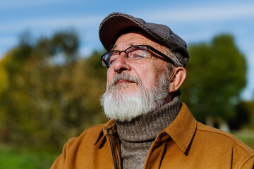 Portrait of handsome older man with a gray beard. Senior standing outdoors in nature, enjoying the...