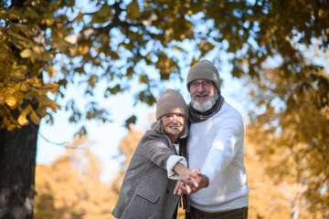 Portrait of beautiful senior couple during walk in autumn park, looking at camera and smiling.