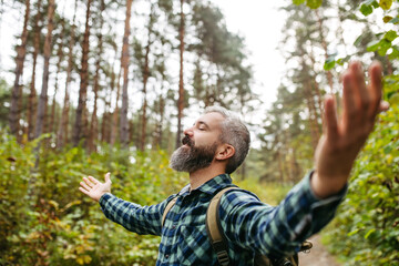 Handsome man standing in the middle of nature with open arms, enjoying peaceful atmosphere of the forest, forestbathing.