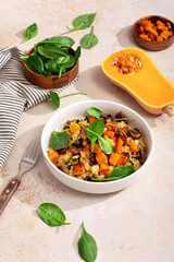 A vegan risotto with roasted pumpkin, mushrooms, and fresh spinach served in a white bowl on a light background