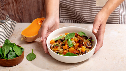 A vegan risotto with roasted pumpkin, mushrooms, and fresh spinach served in a white bowl on a light background
