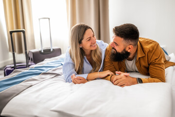 Young happy couple is on vacation. Tourists arrived in hotel room and relaxing on bed.