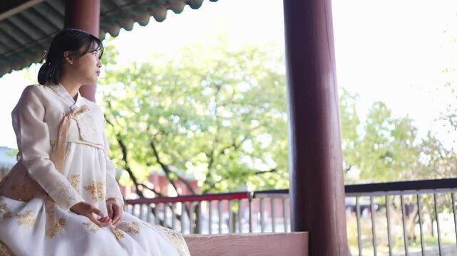 A Korean woman in her 20s wearing a Hanbok sits in a historical building in Seoul, South Korea. Slow motion video.