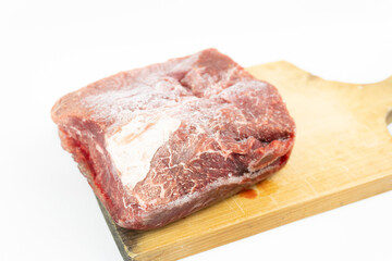 Top view of raw frozen boneless beef piece on cutting board isolated on white background.