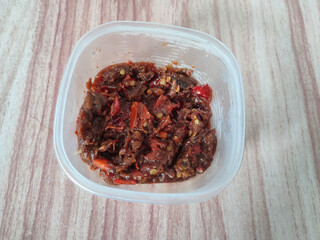 Top view of traditional spicy chili paste in a plastic container on a wooden surface. Perfect for food blogs, culinary concepts, or traditional recipe illustrations.