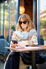 Attractive blond haired woman sitting at a table outside a cafe and using her smartphone