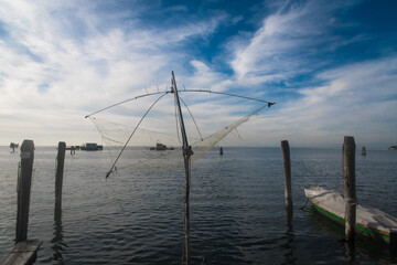 Una rete a bilancia per la pesca sospesa sull&rsquo;acqua della laguna di Venezia a Pellestrina si staglia contro il cielo azzurro e pieno di belle nuvole in una giornata autunnale 