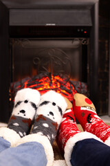 First person view of feet in Christmas socks by the fireplace. A pair of feet in warm Christmas wool socks warming themselves near the fireplace. Christmas atmosphere. Winter, New Year concept