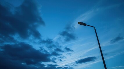 A solitary streetlamp emits soft light under a dramatic blue sky with dark grey clouds and a few wispy strands of cirrus, rustic, blue sky