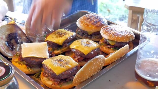 Making burgers and hamburgers outdoor.  Two friends preparing cheesebugres. One of them puts ingridients down and the other grills cheese slices with gas burner