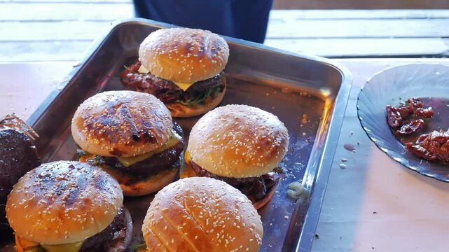 Making burgers and hamburgers outdoor.  Male takes cooked ready grilled cheeseburger from the plate