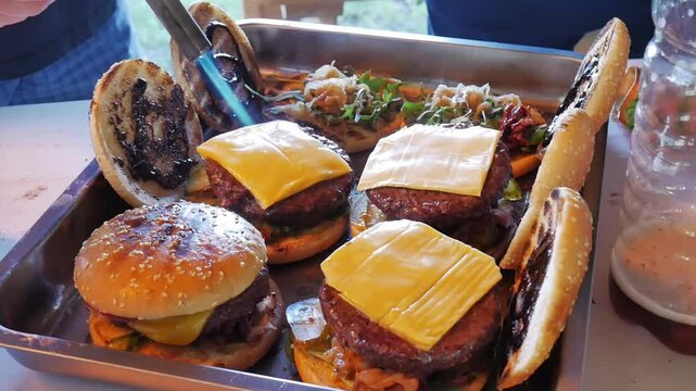 Making burgers and hamburgers outdoor.  Two friends preparing cheesebugres. One of them puts dried tomatoes down and the other grills cheese slices with gas burner