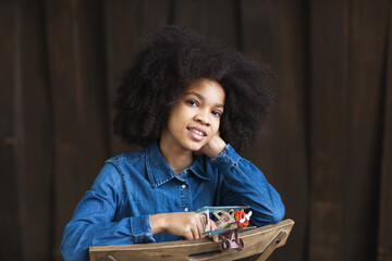 Dreamy smiling african american girl in a denim shirt with an airplane model in her hands. Travel concept.