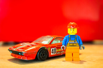 Fototapeta premium Lego toy of a construction worker standing next to his red Ferrari GTO racing car