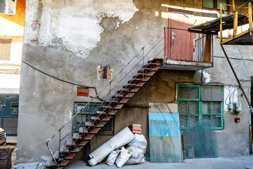 An outdoor staircase in an industrial courtyard with rusted metal steps, a weathered door, peeling...