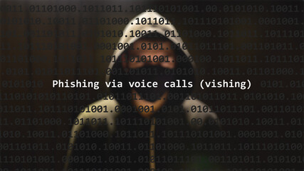 Cyber attack phishing via voice calls (vishing) text in foreground screen, anonymous hacker hidden with hoodie in the blurred background. Vulnerability text in binary system code on editor program.