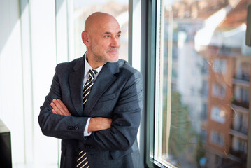 Fototapeta premium Mature businessman standing in a modern office and looking out of the window