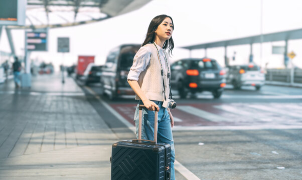 Standing tourist woman with travel luggage waiting at bus terminal for transport on day