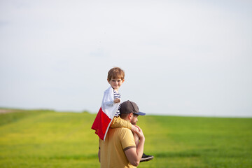 Little boy sitting on father's shoulders wrapped in flag of Poland. Fathers day in Poland. Polish...