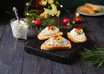 Cold appetizer, mackerel rillettes on white bread toasts on wooden board in Christmas decor on dark...