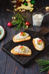 Cold appetizer, mackerel rillettes on white bread toasts on wooden board in Christmas decor on dark wooden background. Holiday appetizers. Recipes fish.