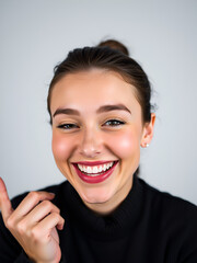 Studio close-up shot of a positive flirtatious young European woman with dark eyes, smiling happily, blinking at the camera in a playful manner, flirting with you.