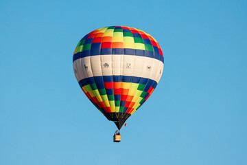 Naklejka premium Whispers of Color: A Vibrant Hot Air Balloon Ascends into the Crisp Blue Sky, Painting Dreams Above the World.