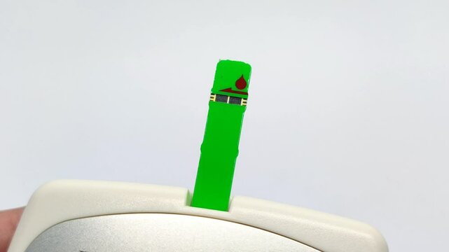 Insert a green blood sugar stick into the device on a white background