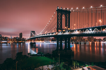 A rooftop view of the Manhattan bridge and the New York City skyline overlooking Brooklyn bridge park during the evening, shot from Dumbo, Brooklyn.