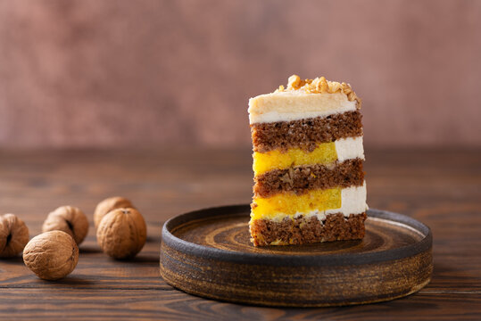 Piece of pumpkin or carrot layered cake with vegan coconut cream and orange confit decorated with walnut in a plate. Sugar, gluten and lactose free.