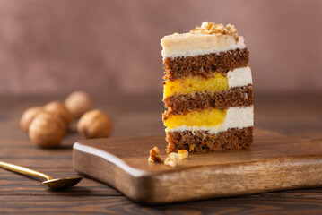 Piece of pumpkin or carrot layered cake with vegan coconut cream and orange confit decorated with walnut in a wooden board. Sugar, gluten and lactose free.