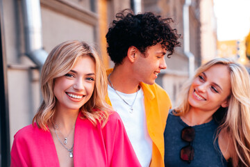 Group of young three stylish friends posing in the street. Fashion man and two cute female dressed in casual summer clothes. Smiling models having fun. Cheerful women and guy outdoors