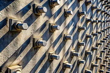 Brutalism Textured metallic wall with bolts and shadows creating a visually striking pattern in natural light.