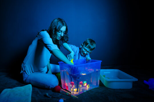 Child and therapist in sensory stimulating room, black snoezelen. Autistic child playing with therapist during occupational therapy session.