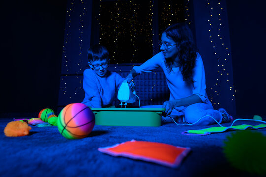 Child and therapist in sensory stimulating room, black snoezelen. Autistic child playing with therapist during occupational therapy session.
