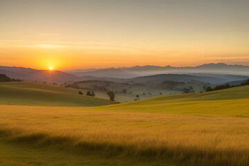 Fototapeta premium A vibrant sunset paints the sky with hues of orange, yellow, and pink, casting a warm glow over rolling hills and a lush, green meadow. The sun dips below the horizon, leaving a trail of light across 