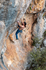 young athletic male climber with long hair climbs an overhanging rock.  muscular young man. a man climbs a very difficult route. extreme sport, outdoor rock climbing