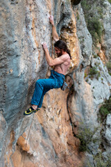 young athletic male climber with long hair climbs an overhanging rock.  muscular young man. a man climbs a very difficult route. extreme sport, outdoor rock climbing