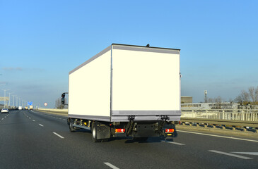 The lorry is driving down the road. Delivering cargo. Furniture transport, space mock up for your design, empty side and backside of the truck box