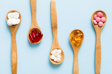 Vitamin capsules in a spoon on a colored background. Pills served as a healthy meal. Red soft gel vitamin supplement capsules on spoon