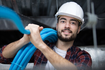 male contractor installing blue pipe in roof space