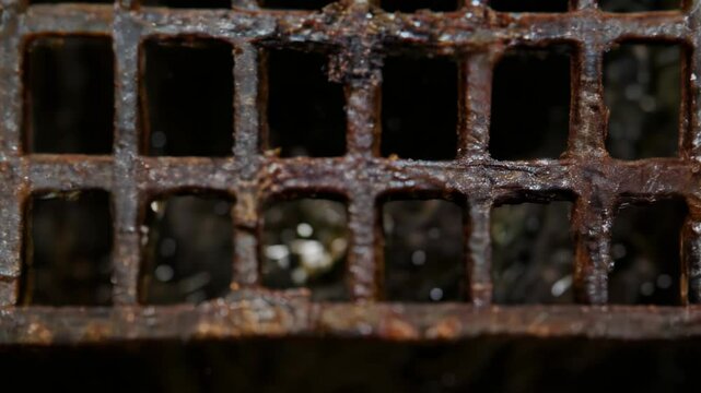 Close-up view of a rusty metal grate with visible corrosion, grime, and uneven texture in a dark industrial environment