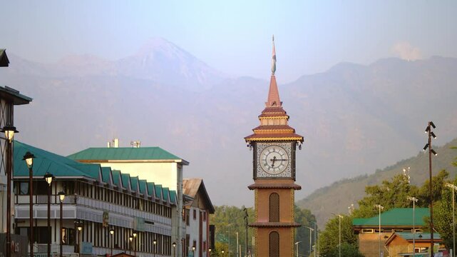 A Close shot of clock tower at Lal chowk surrounded by houses or building with a view of towering snow capped Himalaya mountains visible in the background, Srinagar, Jammu and Kashmir, India