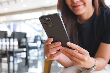 Closeup image of a young woman holding and using mobile phone in cafe