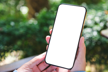 Mockup image of a woman holding mobile phone with blank white desktop screen in the outdoors