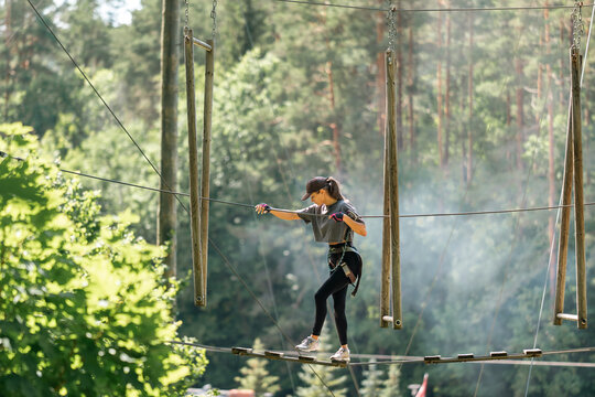 A spirited young girl boldly navigates a challenging high ropes course that is beautifully surrounded by trees