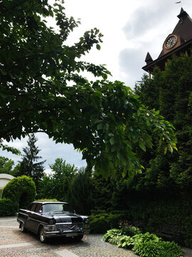 Uzhgorod, Ukraine - May 26, 2021: Classic GAZ Chaika car parked under lush green trees near vintage clock tower