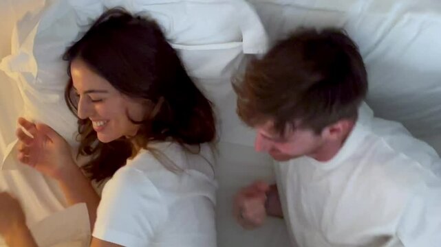 A happy young couple in their cozy bedroom, smiling and relaxing together in a warm ambiance before sleep. A peaceful and harmonious bedtime routine for two young adults. Couple in bed at home