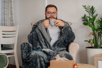 Sick man drinking hot beverage at home using nebulizer for inhalation therapy