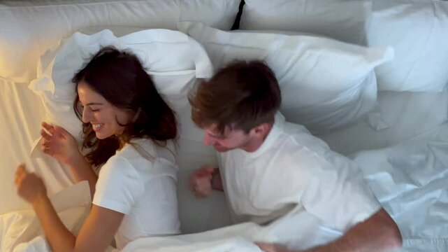 A serene evening scene of a young adult couple lying in bed, smiling and happy, with soft lighting and a cozy atmosphere that emphasizes intimacy and calm. Couple in bed at home happy ready to sleep